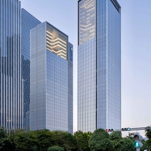 Both towers seen from the street intersection at dusk, the lit atria visible at the top of each crown.