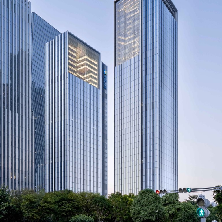 Both towers seen from the street intersection at dusk, the lit atria visible at the top of each crown.