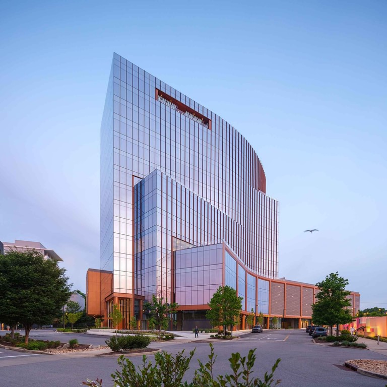 The tower at dusk from the street, its curved glass facade rising above a stepped copper-trimmed base.
