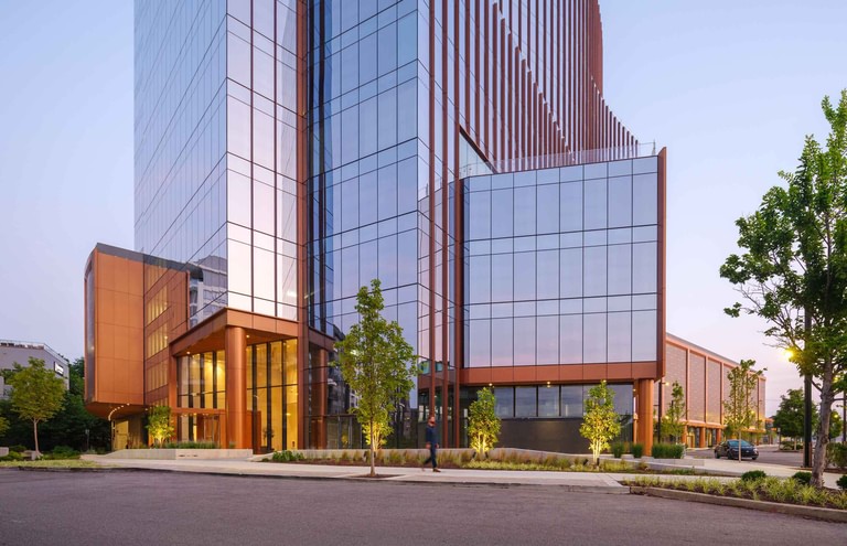 The corner entry at dusk, a copper-clad entry volume with the lit lobby visible behind glass.