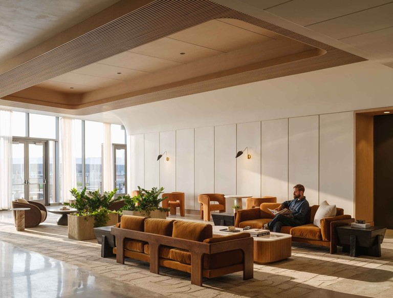 The amenity lounge, curtained glazing and glass doors to the terrace, tan leather seating beneath a coffered wood ceiling.