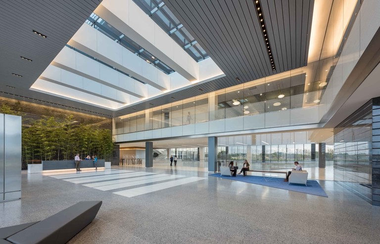The two-story lobby, terrazzo floor and linear ceiling system, glazed on the perimeter with the landscape in view and people seated.