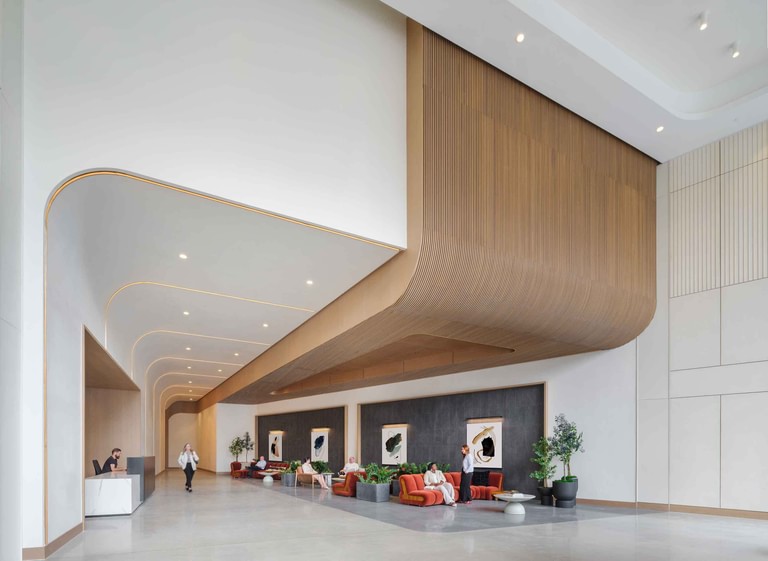 The lobby along its full length, curved white soffits and a ribbed wood ceiling volume with reception at the far end.