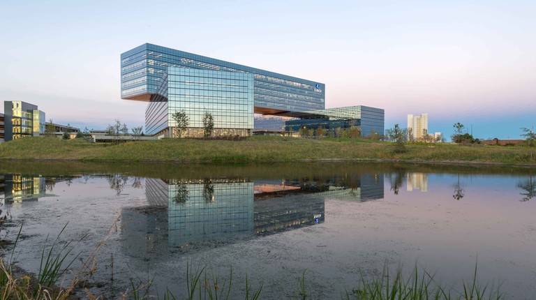 The full silhouette of the three bars mirrored in a retention basin at dusk, native prairie grasses in the foreground.