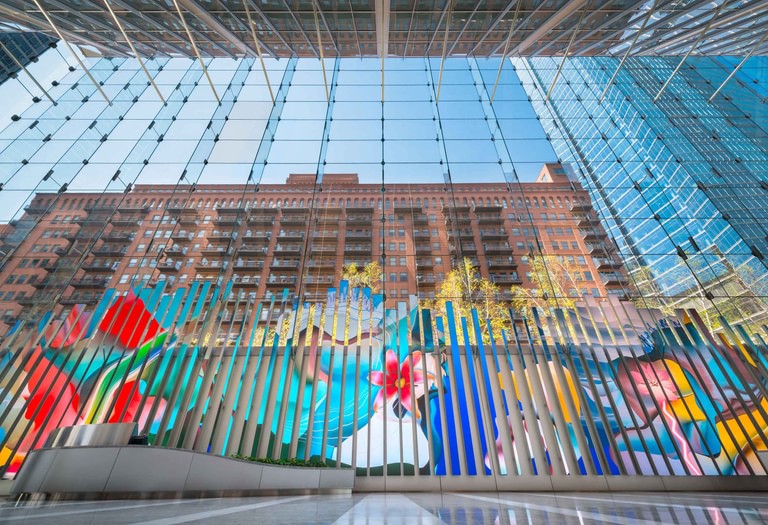 Looking up through the suspended glass-fin wall from inside the lobby, spider fittings and mullions against the sky.