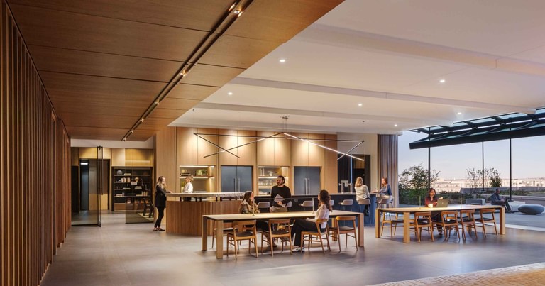 The pantry and communal table on the amenity level, wood-slat walls and a warm ceiling, with the glass wall open to the terrace beyond.