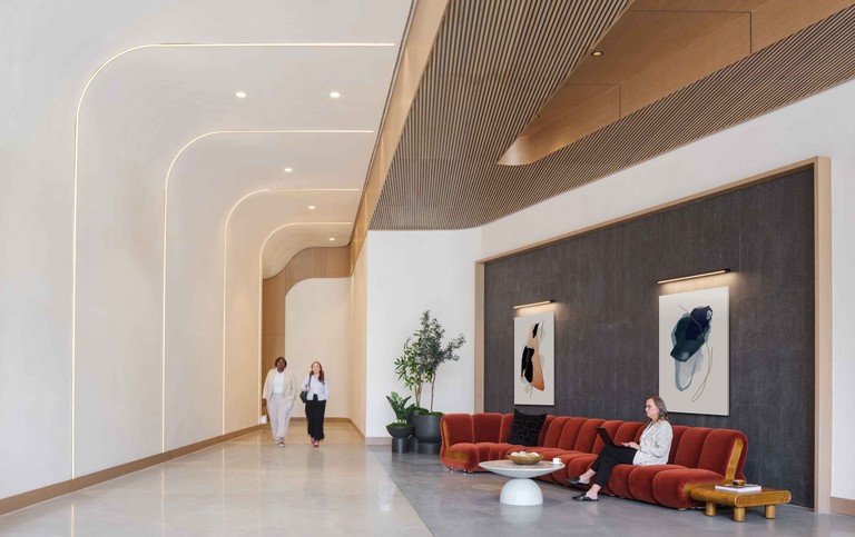 The lobby's layered ceiling reveals seen closer in, lit along each edge, above a red seating group and framed artwork.