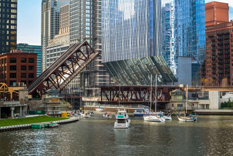 River level with a bascule bridge raised in the foreground and the building's glazed underside lifting beyond it.