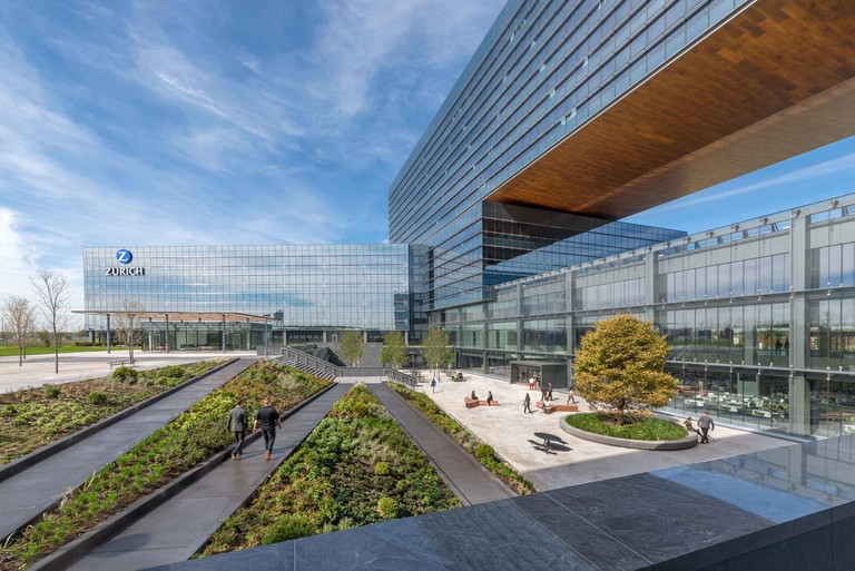 The courtyard between the bars, the cantilever overhead and terraced planting beds running through the plaza with people walking.
