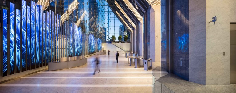 The lobby at the turnstiles, the media blades lit blue and people crossing the terrazzo in motion.