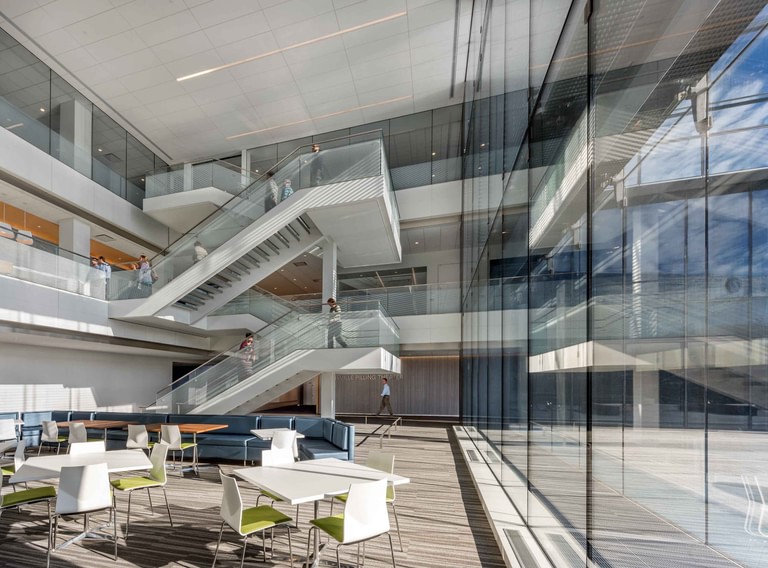 The open stair rising through the glazed volume, with collaboration seating in the foreground.