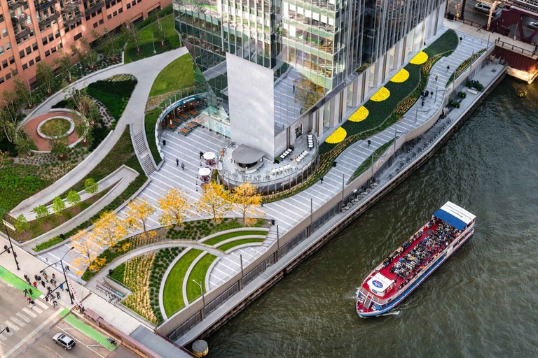The park seen from above, paths and planting sweeping around the building's core with the riverwalk along the water's edge.