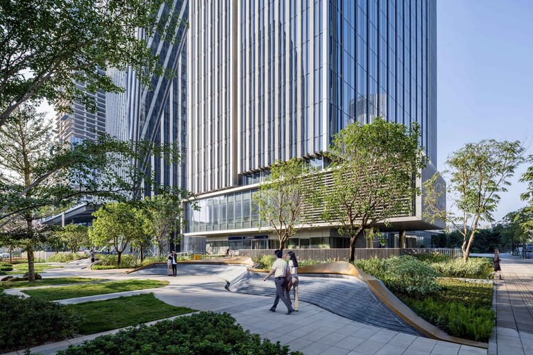 Landscaped walks and planted beds at the base of the towers, with a shaded terrace under a metal trellis.