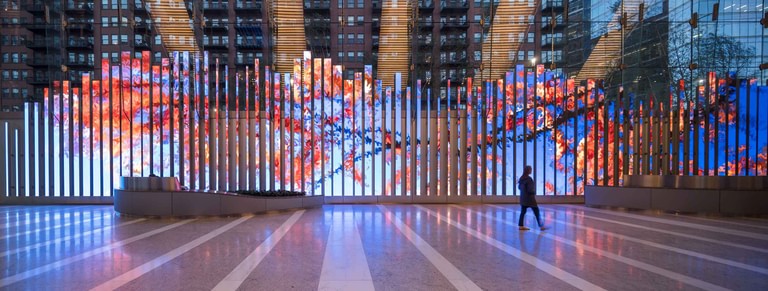 The media blades in bloom across the lobby wall, a single figure crossing the floor.