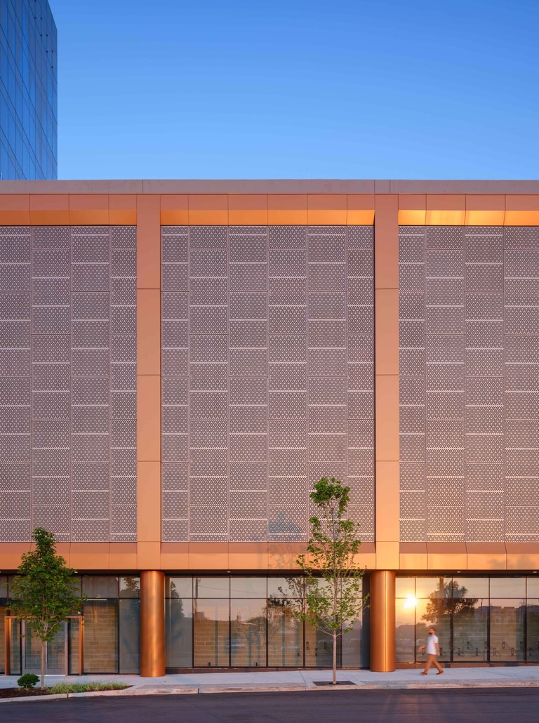 The parking structure elevation, perforated metal panels in a patterned field between copper mullions above a glass retail base.