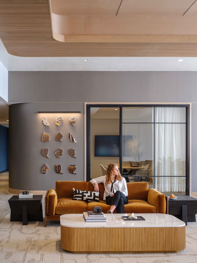 An amenity seating group, sculptural wall pieces mounted on a curved wall beside sliding glass to a meeting room.