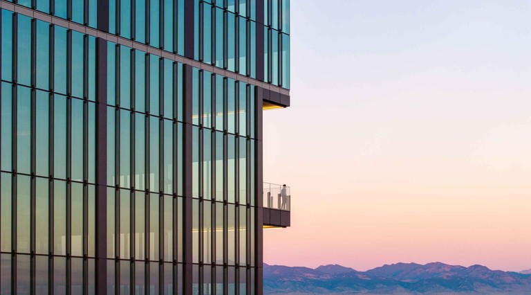 Facade detail at sunset, the glass grading from green to rose with a terrace edge at the corner and the Front Range beyond.