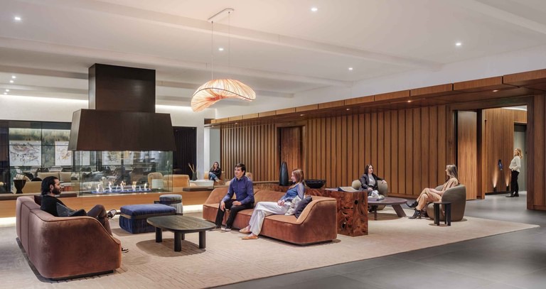 The hospitality lounge, a black hood over the hearth and a woven pendant above lounge seating on rugs, with people gathered.