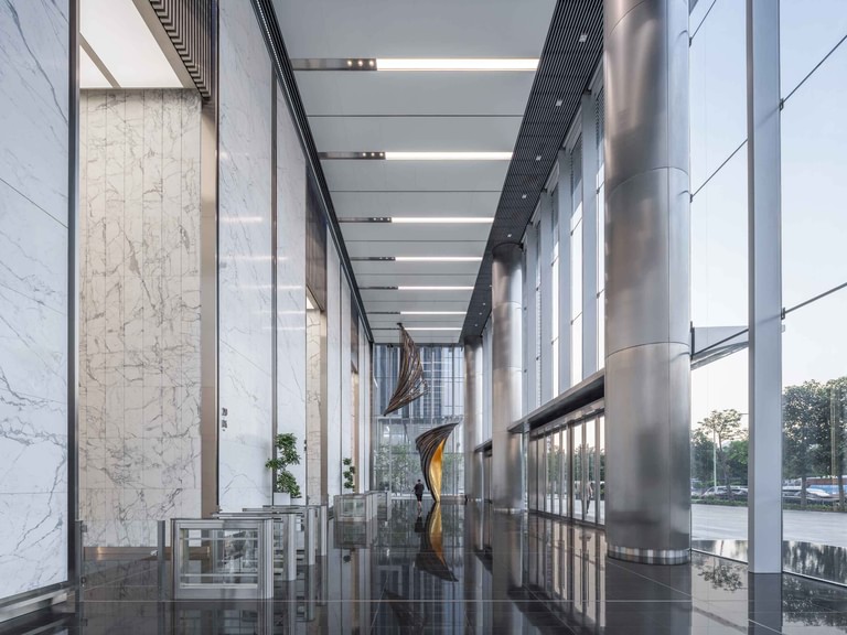 The ground-floor lobby, with white marble walls, stainless-clad columns and a suspended bronze sculpture.
