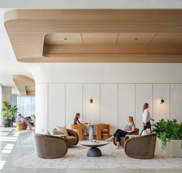 A lounge beneath a ribbed wood ceiling cloud, swivel chairs and banquette work nooks in use.