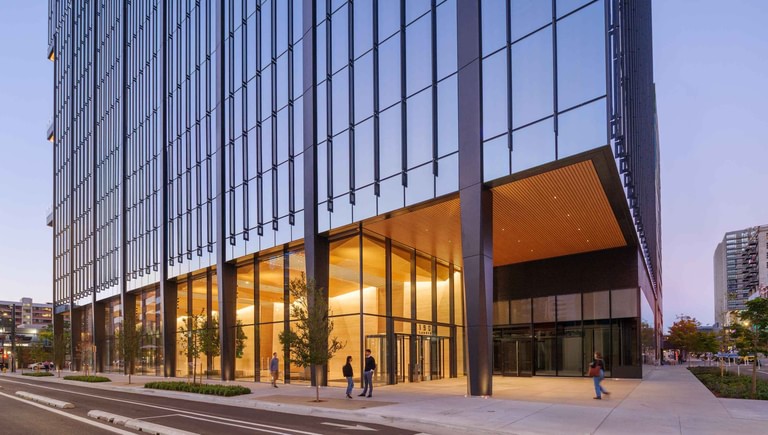 The lobby running the full 19th Street block behind a deep projecting canopy, warm-lit through full-height glass at dusk.
