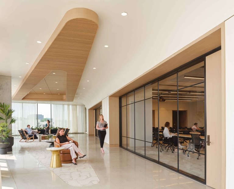 The corridor past a glass-walled training room in use, with lounge seating and curtained glazing beyond.