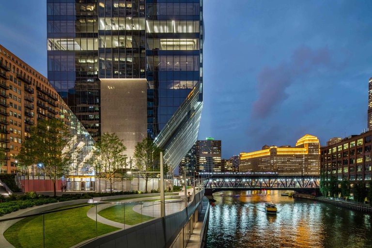Dusk from the elevated park, glass balustrade and lit riverwalk with the city across the water.