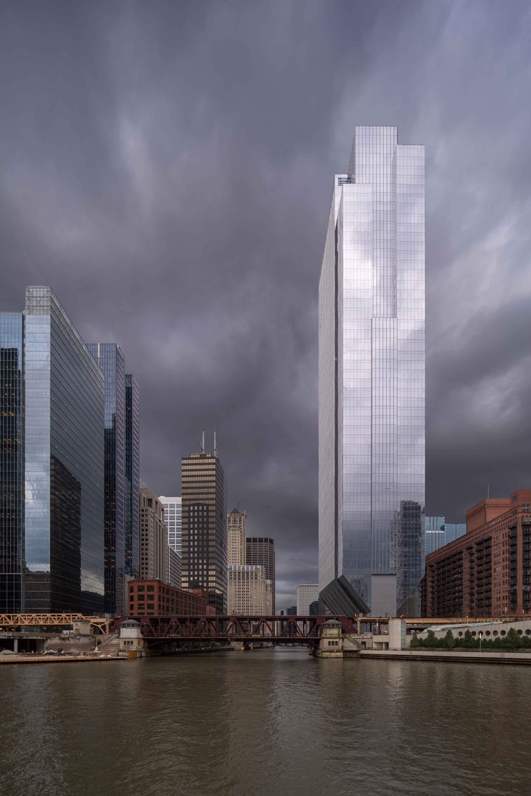 The tower from downriver under a storm sky, its sculpted crown and tapered base above the bridges.